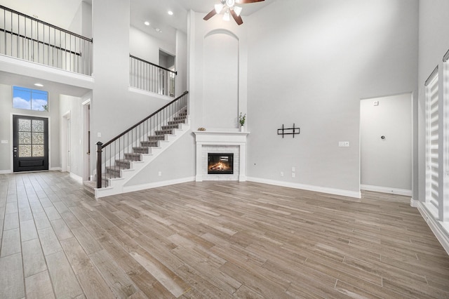 28702 Casen Ranch Ln, Fulshear, TX 77441 - unfurnished living room with a high ceiling, wood finished floors, a ceiling fan, stairway, and a brick fireplace