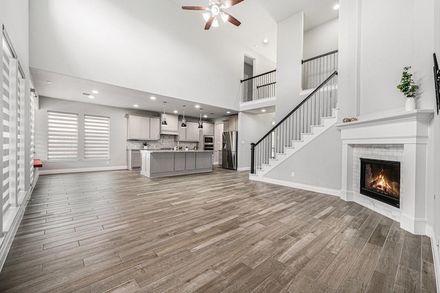 28702 Casen Ranch Ln, Fulshear, TX 77441 - unfurnished living room featuring light wood-type flooring, a ceiling fan, a towering ceiling, a brick fireplace, and stairway