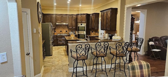 5322 Norborne Ln, Houston, TX 77069 - kitchen with stainless steel appliances, a peninsula, dark brown cabinetry, a breakfast bar area, and backsplash