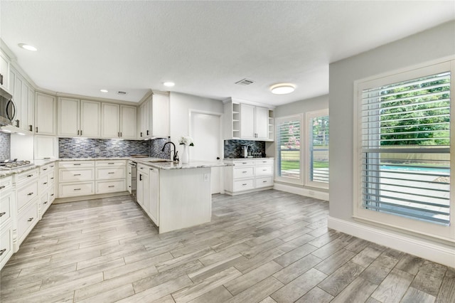 1904 Nursery Rd, The Woodlands, TX 77380 - kitchen with open shelves, decorative backsplash, stainless steel appliances, light wood-type flooring, and light stone counters