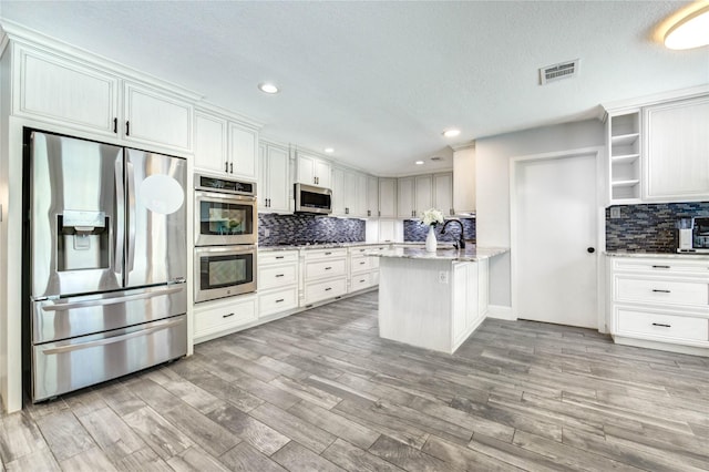 1904 Nursery Rd, The Woodlands, TX 77380 - kitchen with stainless steel appliances, a peninsula, light wood finished floors, decorative backsplash, and white cabinets