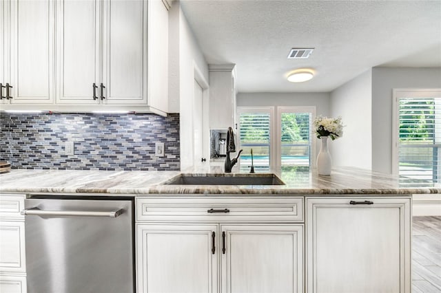 1904 Nursery Rd, The Woodlands, TX 77380 - kitchen featuring stainless steel dishwasher, white cabinetry, backsplash, light stone counters, and a textured ceiling