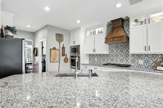 14506 Heron Marsh Dr, Cypress, TX 77429 - kitchen featuring stainless steel appliances, premium range hood, light stone countertops, white cabinetry, and decorative backsplash