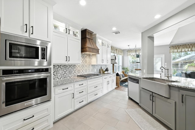 14506 Heron Marsh Dr, Cypress, TX 77429 - kitchen with appliances with stainless steel finishes, custom range hood, light tile patterned flooring, tasteful backsplash, and glass insert cabinets