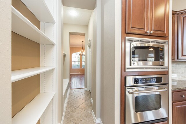 18219 S Austin Shore Dr, Cypress, TX 77433 - kitchen with appliances with stainless steel finishes, light tile patterned floors, a chandelier, backsplash, and brown cabinets