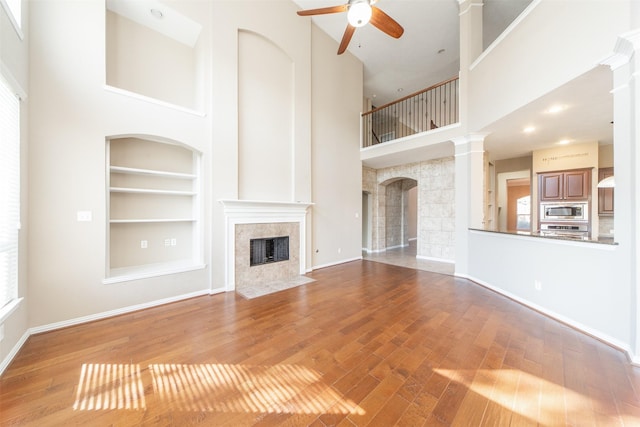 18219 S Austin Shore Dr, Cypress, TX 77433 - unfurnished living room featuring a high end fireplace, built in shelves, a towering ceiling, ceiling fan, and hardwood / wood-style flooring