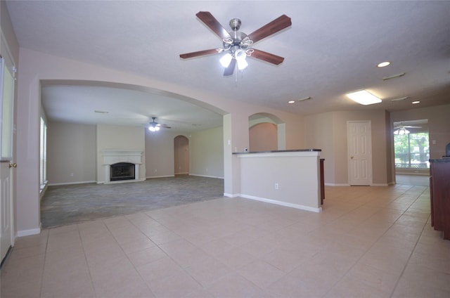 6906 Grant Dr, Magnolia, TX 77354 - unfurnished living room featuring ceiling fan, arched walkways, light tile patterned floors, a fireplace with raised hearth, and recessed lighting