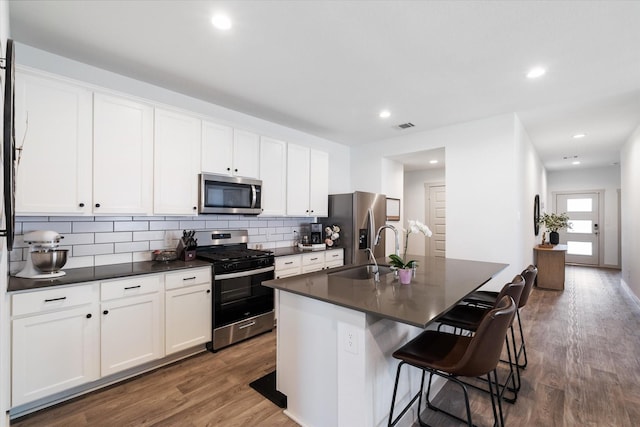 14906 Rain Tree Dr, Baytown, TX 77523 - kitchen with appliances with stainless steel finishes, dark countertops, an island with sink, dark wood-style flooring, and backsplash