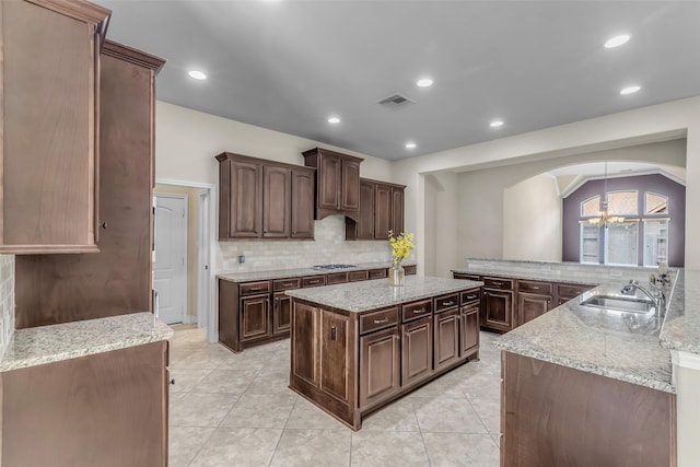 2206 Chelsea Creek Ln, Spring, TX 77386 - kitchen featuring arched walkways, decorative backsplash, a center island, stainless steel gas cooktop, and a chandelier