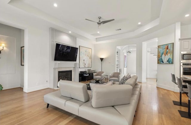 7526 Janak Dr, Houston, TX 77055 - living room with a raised ceiling, a ceiling fan, a fireplace with flush hearth, light wood-style floors, and recessed lighting
