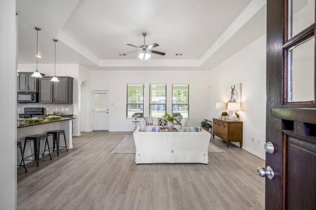 16070 Deer Pines Dr, Conroe, TX 77303 - living room featuring a tray ceiling, a ceiling fan, arched walkways, and light wood-style flooring