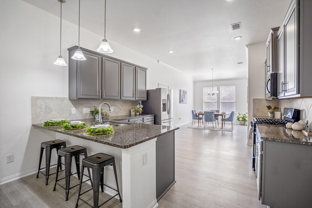16070 Deer Pines Dr, Conroe, TX 77303 - kitchen with stainless steel appliances, dark stone counters, light wood-style flooring, decorative backsplash, and a peninsula