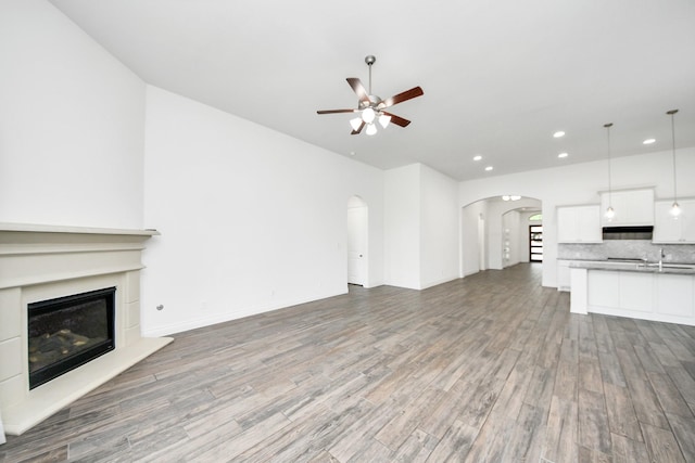 28430 Sycamore Falls Ln, Fulshear, TX 77441 - unfurnished living room with arched walkways, a ceiling fan, recessed lighting, wood finished floors, and a glass covered fireplace