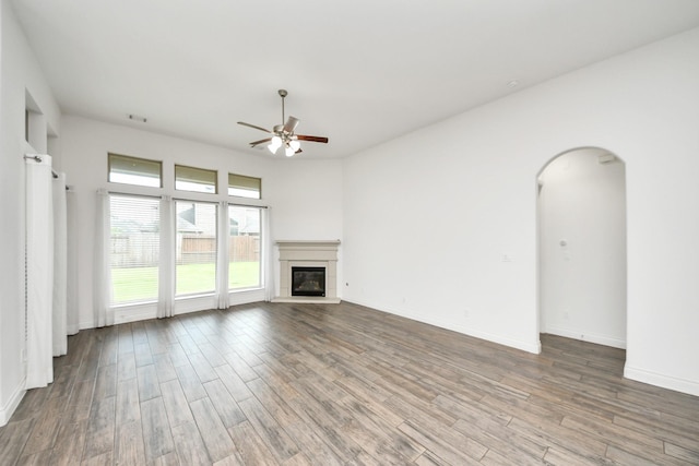 28430 Sycamore Falls Ln, Fulshear, TX 77441 - unfurnished living room with a ceiling fan, wood finished floors, arched walkways, and a glass covered fireplace