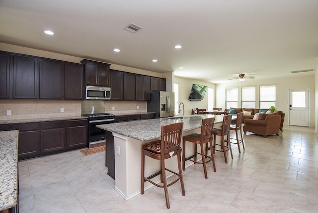 4302 Lisboa Cir, Katy, TX 77493 - kitchen featuring stainless steel appliances, a kitchen bar, a ceiling fan, backsplash, and an island with sink
