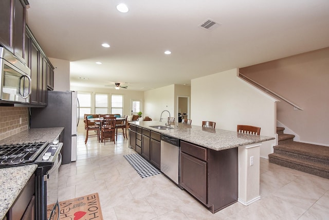 4302 Lisboa Cir, Katy, TX 77493 - kitchen with stainless steel appliances, a ceiling fan, a kitchen island with sink, dark brown cabinetry, and recessed lighting