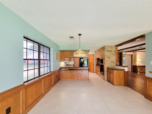 3 Thunderbird Cir, Baytown, TX 77521 - kitchen featuring black appliances, a peninsula, brown cabinets, a textured ceiling, and a wainscoted wall