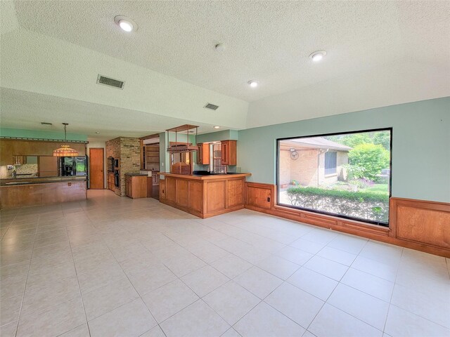 3 Thunderbird Cir, Baytown, TX 77521 - kitchen with brown cabinets, a wainscoted wall, a textured ceiling, a peninsula, and open floor plan