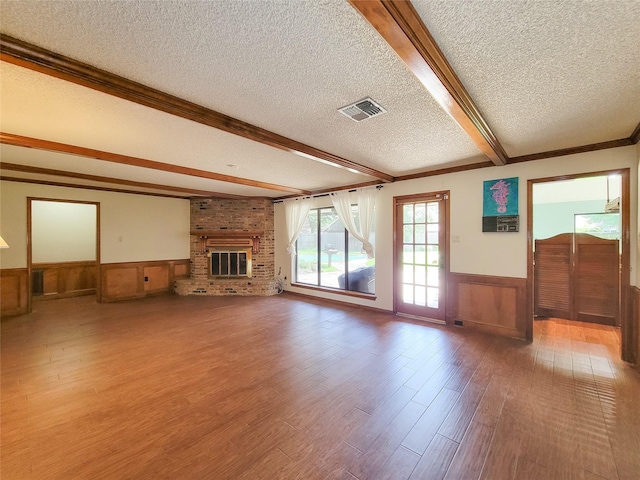 3 Thunderbird Cir, Baytown, TX 77521 - unfurnished living room with a textured ceiling, wainscoting, wood finished floors, beamed ceiling, and a brick fireplace