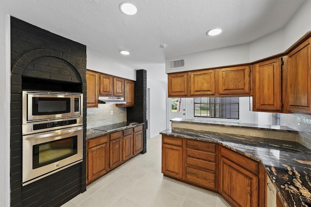 12611 Old River Dr, Baytown, TX 77523 - kitchen featuring stainless steel appliances, under cabinet range hood, brown cabinetry, backsplash, and dark stone counters