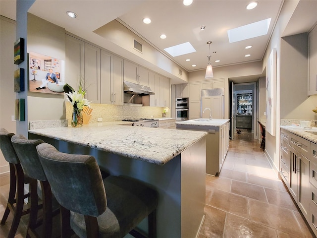 3124 Mid Ln, Houston, TX 77027 - kitchen featuring a skylight, under cabinet range hood, a kitchen island with sink, backsplash, and a peninsula