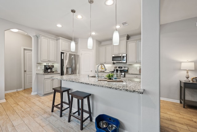 16863 Big Reed Dr, Humble, TX 77346 - kitchen with appliances with stainless steel finishes, light wood-style floors, backsplash, light stone counters, and a breakfast bar