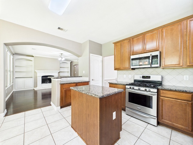 8122 Silver Lure Dr, Humble, TX 77346 - kitchen featuring stainless steel appliances, a kitchen island, light stone counters, brown cabinetry, and light tile patterned floors