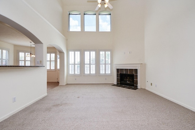 150 Nina Ln, Stafford, TX 77477 - unfurnished living room with a ceiling fan, carpet flooring, a tile fireplace, arched walkways, and a high ceiling