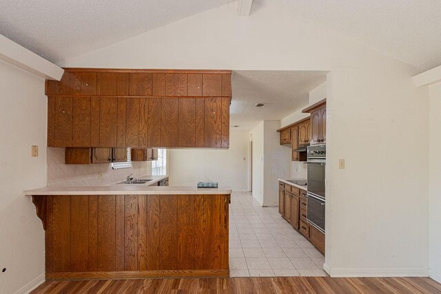 8111 Dellanera Dr, Hitchcock, TX 77563 - kitchen featuring lofted ceiling, a peninsula, light countertops, brown cabinetry, and multiple ovens