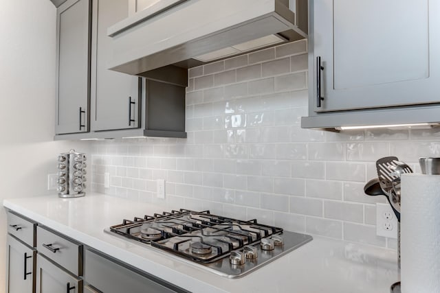 6907 Pondhawk Dr, Katy, TX 77493 - kitchen featuring stainless steel gas stovetop, wall chimney exhaust hood, gray cabinetry, light countertops, and backsplash