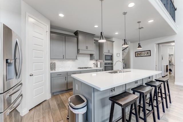 6907 Pondhawk Dr, Katy, TX 77493 - kitchen with appliances with stainless steel finishes, gray cabinetry, a breakfast bar area, decorative backsplash, and light wood-style floors