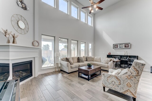 6907 Pondhawk Dr, Katy, TX 77493 - living room featuring a towering ceiling, ceiling fan, a glass covered fireplace, and wood finished floors