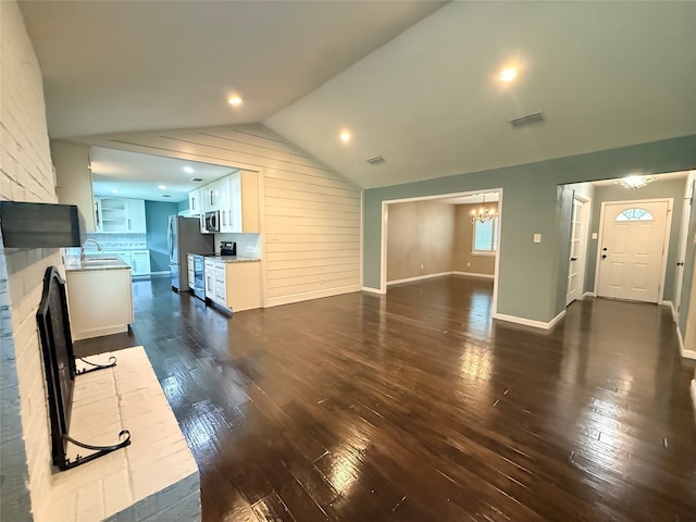 1502 Robin St, Mineola, TX 75773 - unfurnished living room with a chandelier, dark wood-type flooring, lofted ceiling, wood walls, and a brick fireplace