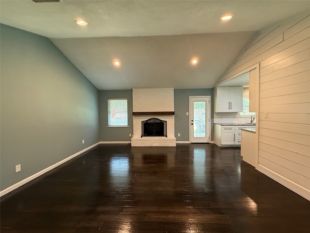 1502 Robin St, Mineola, TX 75773 - unfurnished living room featuring vaulted ceiling, dark wood-style floors, a brick fireplace, recessed lighting, and wooden walls