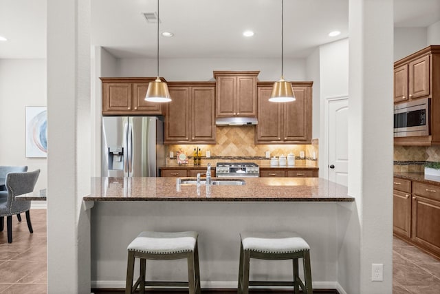 14 Painted Post Pl, The Woodlands, TX 77389 - kitchen featuring stainless steel appliances, under cabinet range hood, a breakfast bar, tasteful backsplash, and dark stone counters