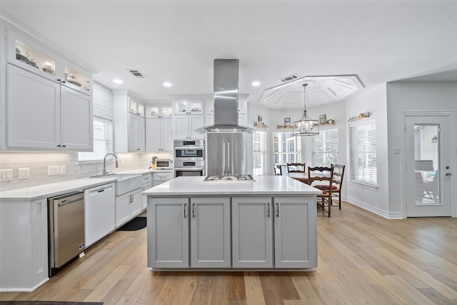 6602 Ranch Park Dr, Magnolia, TX 77354 - kitchen featuring appliances with stainless steel finishes, light countertops, island exhaust hood, tasteful backsplash, and light wood-type flooring