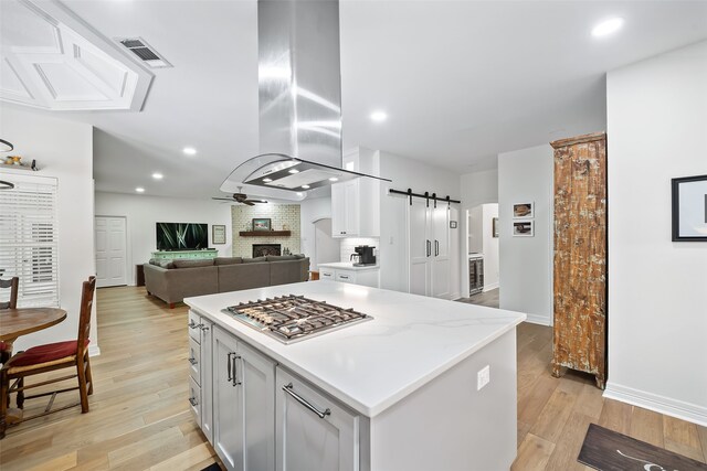 6602 Ranch Park Dr, Magnolia, TX 77354 - kitchen with stainless steel gas stovetop, island exhaust hood, ceiling fan, a barn door, and light wood-type flooring