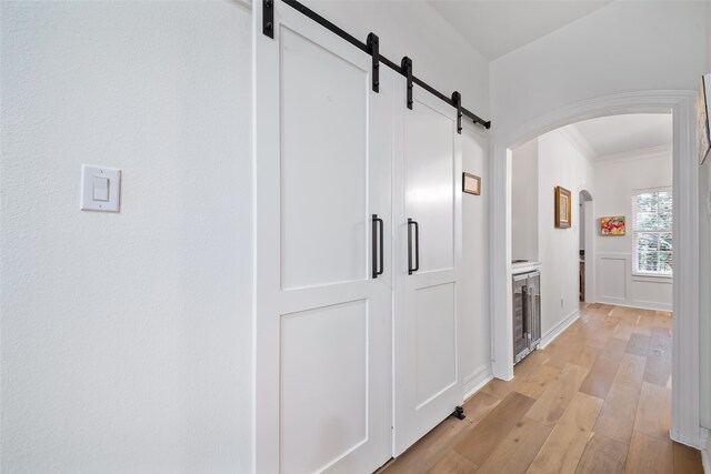 6602 Ranch Park Dr, Magnolia, TX 77354 - hall featuring a barn door, arched walkways, light wood-style flooring, wine cooler, and ornamental molding