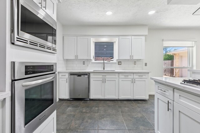 11406 Meadow Lake Dr, Houston, TX 77077 - kitchen featuring appliances with stainless steel finishes, a textured ceiling, light countertops, white cabinets, and backsplash