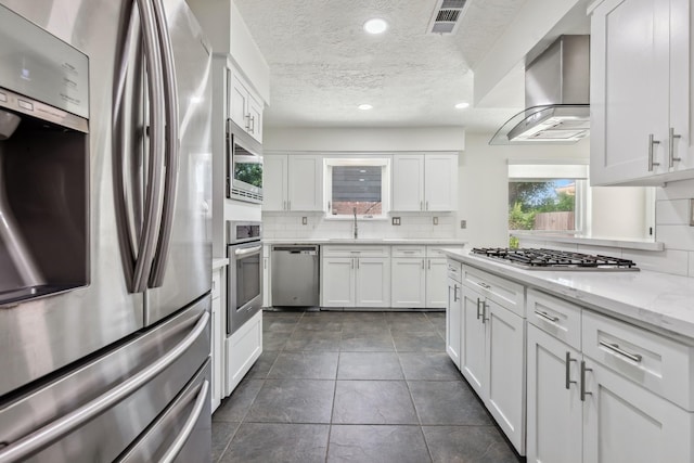 11406 Meadow Lake Dr, Houston, TX 77077 - kitchen featuring stainless steel appliances, wall chimney exhaust hood, tasteful backsplash, a textured ceiling, and white cabinets