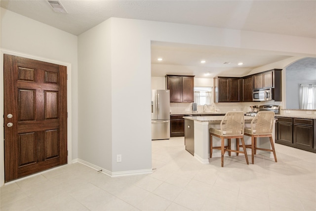 115 Meadow Ridge Way, Clute, TX 77531 - kitchen featuring refrigerator with ice dispenser, stainless steel microwave, range, dark brown cabinetry, and a kitchen breakfast bar