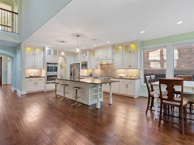 4635 Beech St, Bellaire, TX 77401 - kitchen featuring stainless steel appliances, arched walkways, dark countertops, a breakfast bar, and backsplash