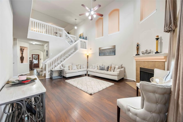 9859 Clanton Pines Dr, Humble, TX 77396 - living room with stairs, a ceiling fan, dark wood-style flooring, a fireplace, and a high ceiling