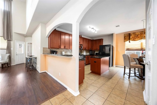 9859 Clanton Pines Dr, Humble, TX 77396 - kitchen featuring stainless steel appliances, decorative backsplash, dark countertops, light tile patterned flooring, and a kitchen island