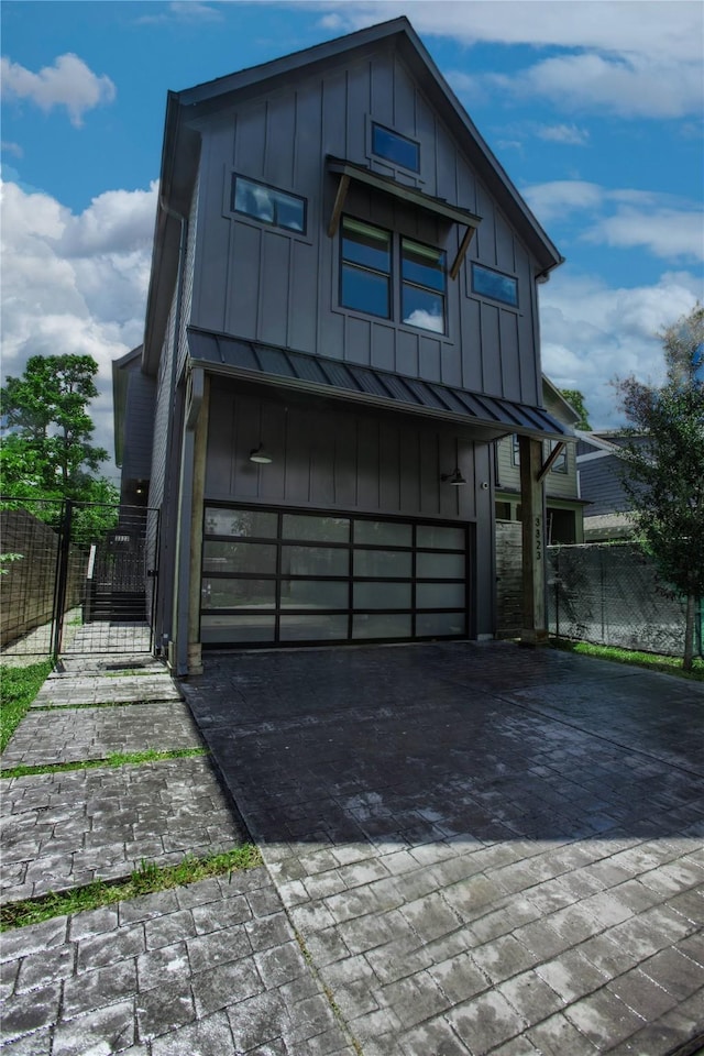 3323 Cornell St, Houston, TX 77022 - modern home with board and batten siding, an attached garage, a gate, decorative driveway, and a standing seam roof