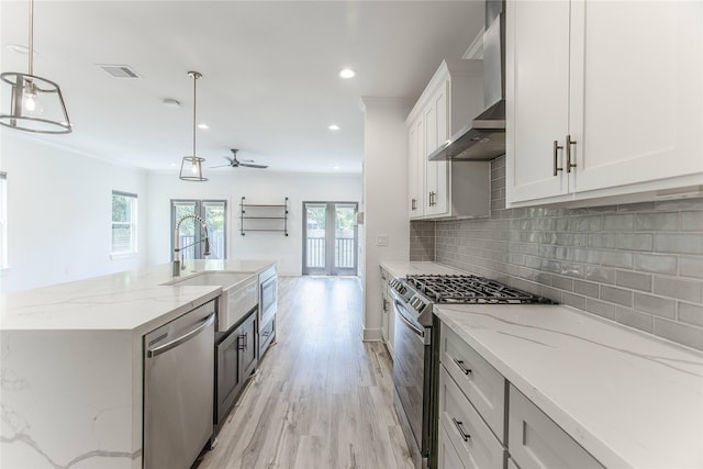 3323 Cornell St, Houston, TX 77022 - kitchen featuring appliances with stainless steel finishes, wall chimney range hood, a ceiling fan, backsplash, and light wood finished floors