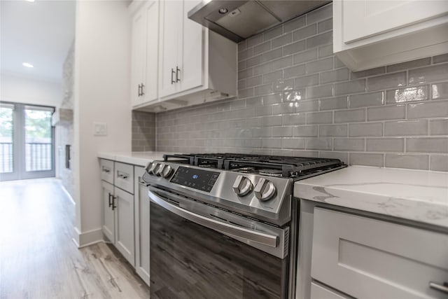 3323 Cornell St, Houston, TX 77022 - kitchen with stainless steel range with gas cooktop, range hood, light stone counters, white cabinets, and light wood-style floors