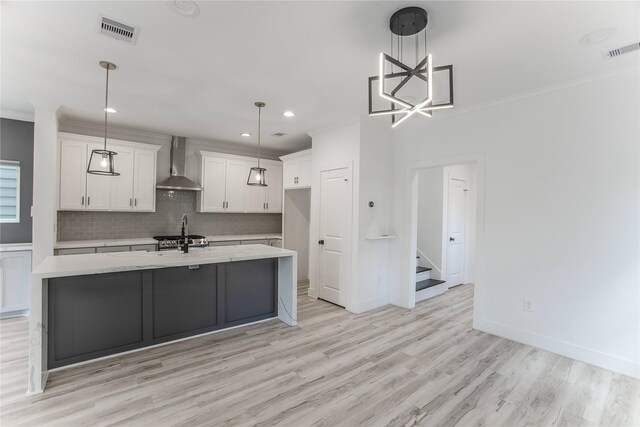 3323 Cornell St, Houston, TX 77022 - kitchen with wall chimney range hood, white cabinetry, ornamental molding, a kitchen island with sink, and light wood-style floors
