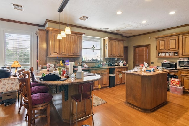 8414 Atascocita Lake Way, Humble, TX 77346 - kitchen featuring stainless steel microwave, light wood finished floors, brown cabinets, ornamental molding, and recessed lighting