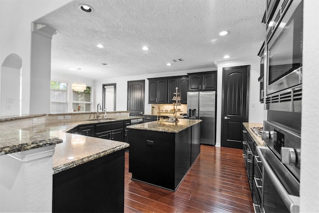 2523 Watts St, Houston, TX 77030 - kitchen with stainless steel appliances, an island with sink, dark wood finished floors, a textured ceiling, and light stone countertops